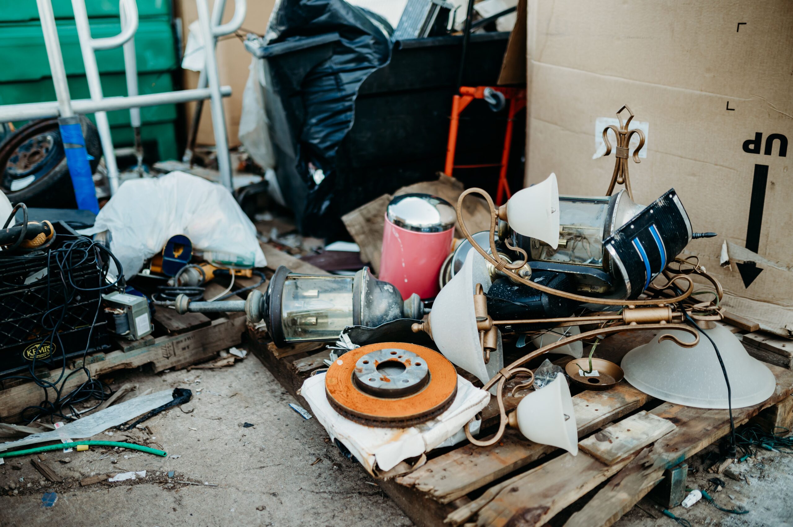Collection of old and used household items including lamps, wires, and furniture remnants scattered in a recycling center, illustrating the clutter often encountered during cleanouts.